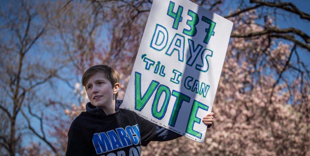 A young man holds up a sign at a rally that reads, "437 days til I can vote."