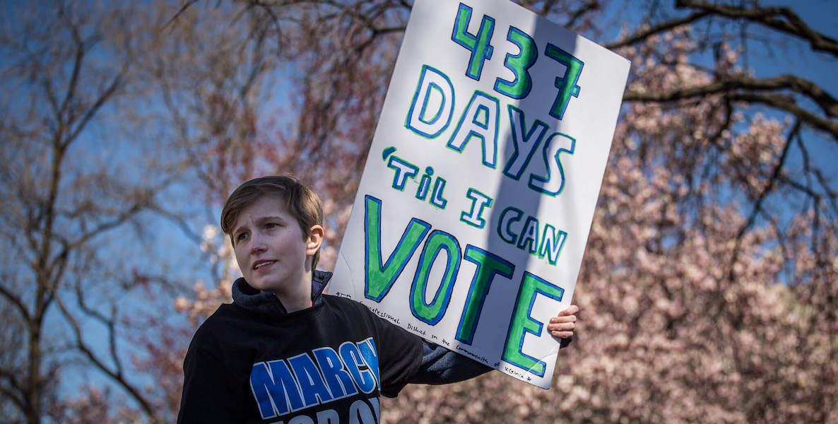 A young man holds up a sign at a rally that reads, "437 days til I can vote."