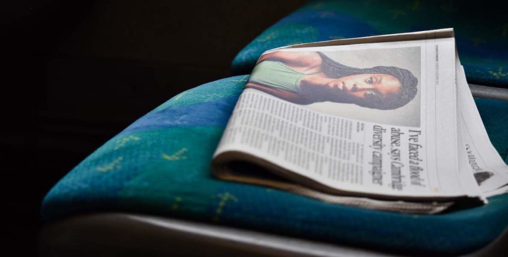 A newspaper emblazoned with a photo of a young black woman sits alone on a seat.