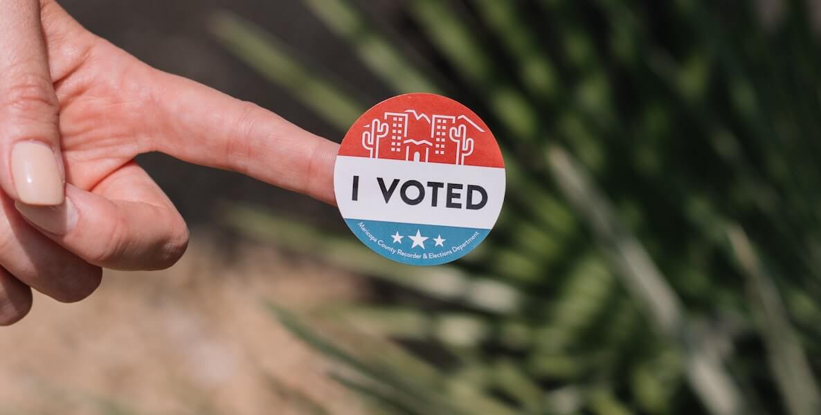 A person holds out an "I Voted" sticker after voting with a voter guide on election day.