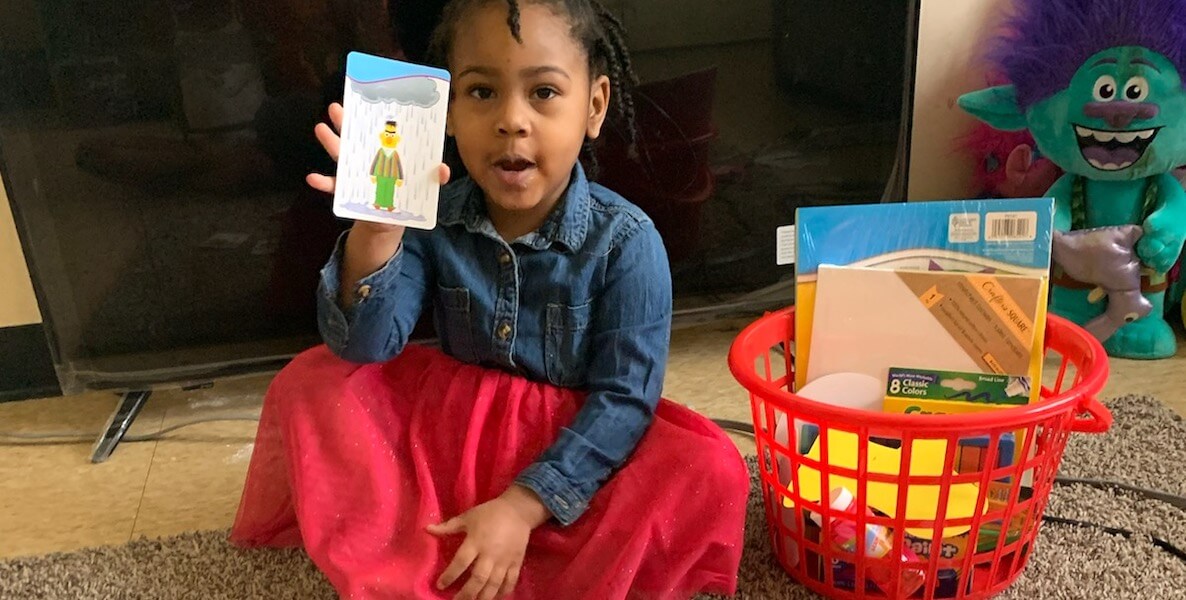 A child in the ParentChild+ program in Philadelphia holds up some flash cards on the floor in her home.