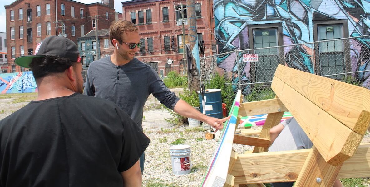 Developer Chadwick Smith looks at a freshly painted picnic table alongside Christian Rodriguez at Sunflower Philly