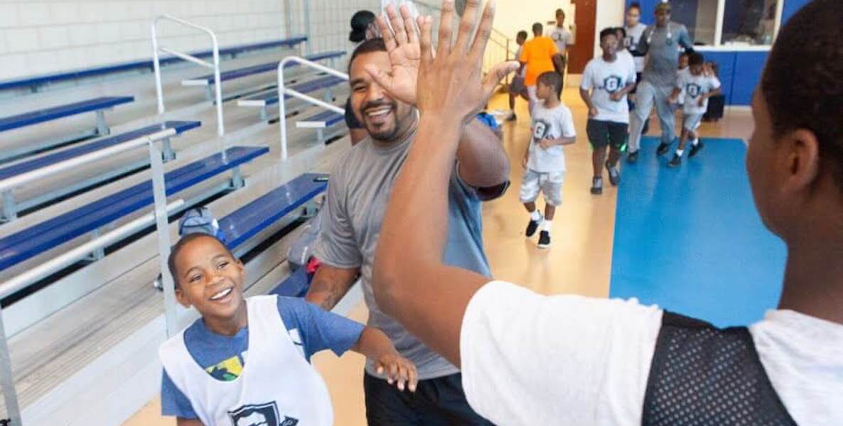 A father and a coach high five as their son looks on at a Give and Go Athletics sporting event