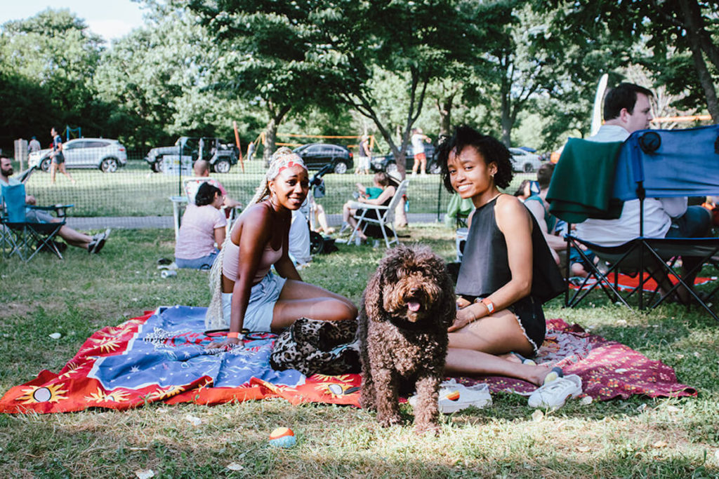 Two friends and their dog sprawl out on a picnic blanket at the FDR Park location of Parks on Tap in Philadelphia