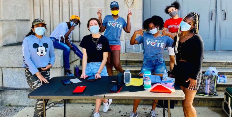 A group of students wearing mask man a table where they are registering people—especially fellow students—to vote.