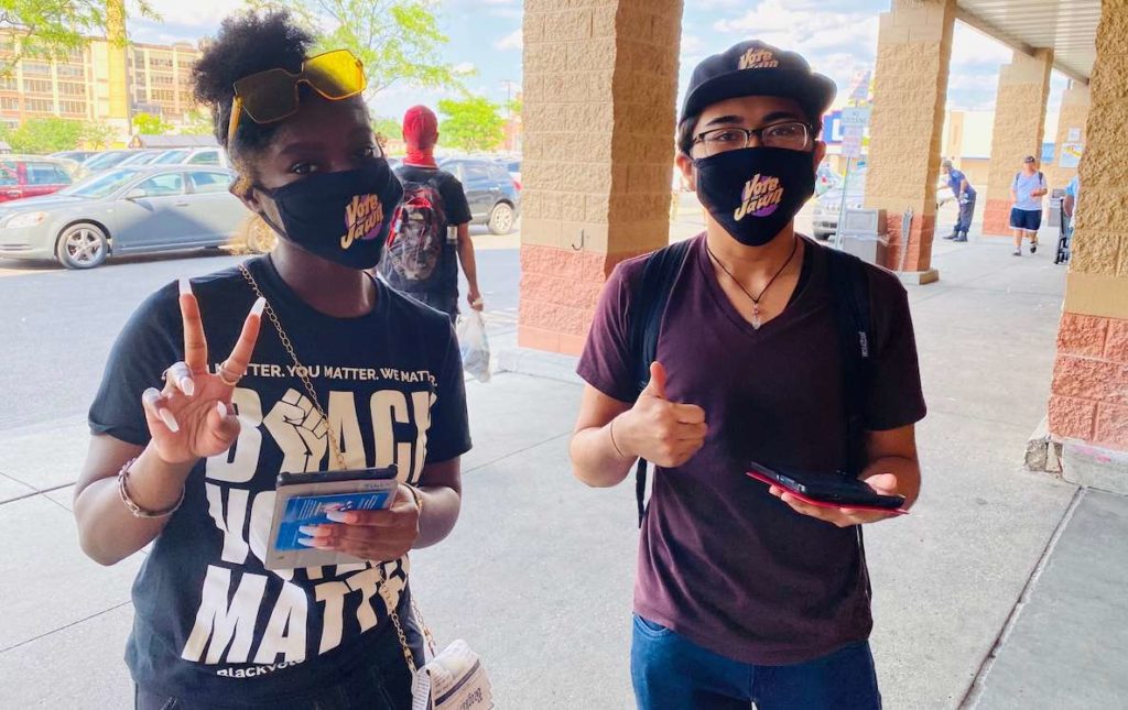 Two Philadelphia students wearing "Vote That Jawn" masks hold tablets that they're using to register student voters.