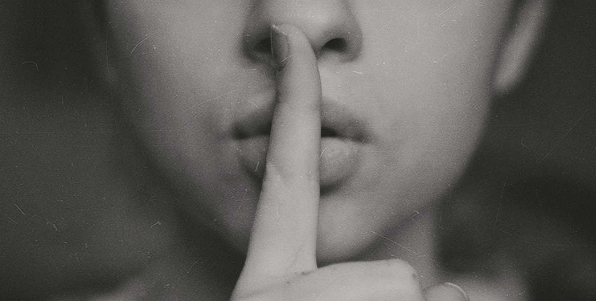 A black and white photo shows a woman with her finger up to her lips, shushing whomever is talking too much. Hush! Hush! I tell you.