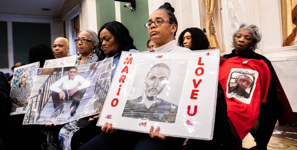 Philadelphia mothers who lost sons to police brutality hold up signs at a special committee on gun violence prevention