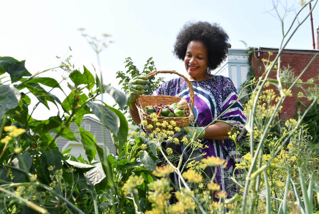 A Philadelphia garder shows off a bounty of produce that she grew in her urban garden, beautiful yellow flowers frame the screen in the foreground.