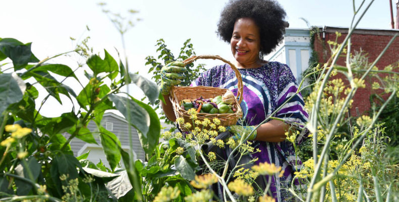 A Philadelphia garder shows off a bounty of produce that she grew in her urban garden, beautiful yellow flowers frame the screen in the foreground.