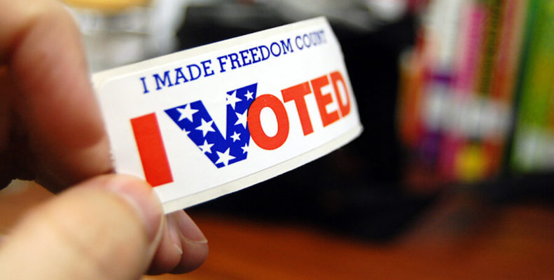 A person holds up a sticker that reads "I made freedom count. I voted."