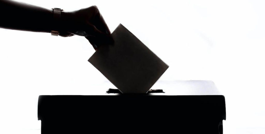 A shadowed hand drops a ballot into the ballot box on election day