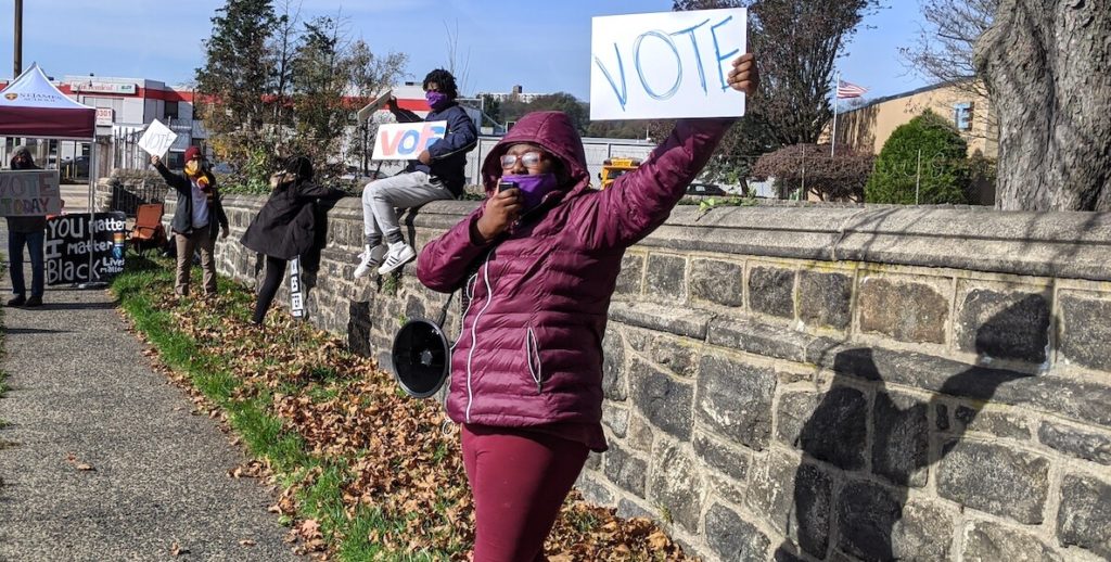 A young woman holds up a sign on the side of a highway in Philadelphia that reads, "Vote!"