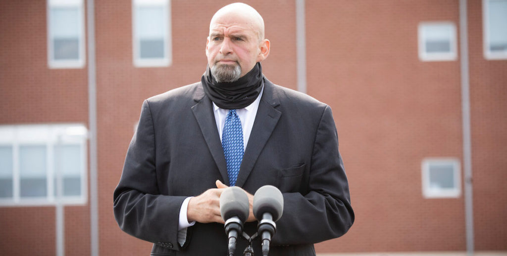 Pennsylvania Lieutenant Governor John Fetterman stands at a podium with a Covid mask around his neck