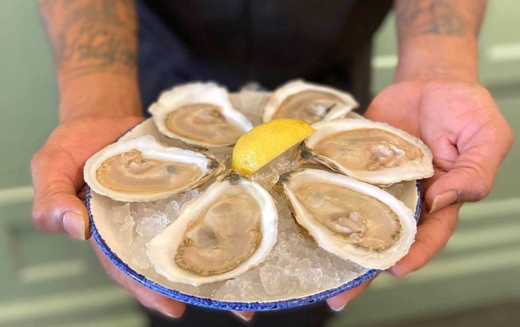 A waiter at Oyster House presents a plate of oysters garnished with a lemon peel