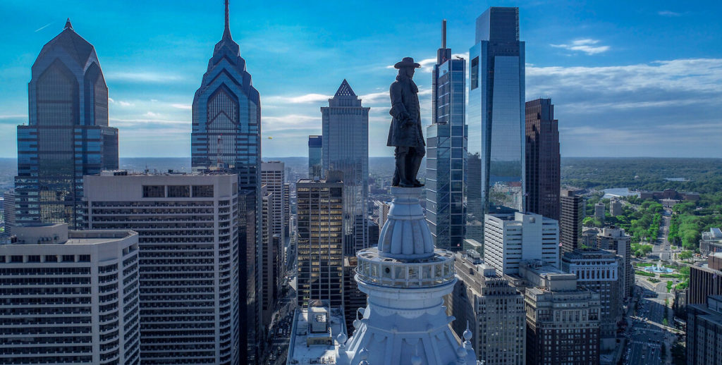The William Penn statue on top of City Hall sits in the foreground of a sweeping view of the Philadelphia skyline