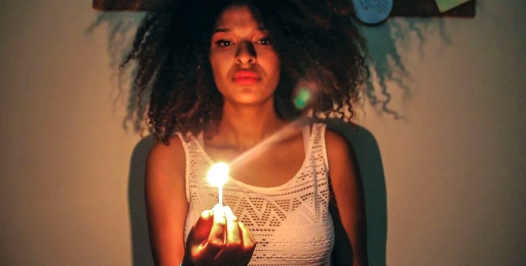 A young woman holds a candle in her hand in a dark room