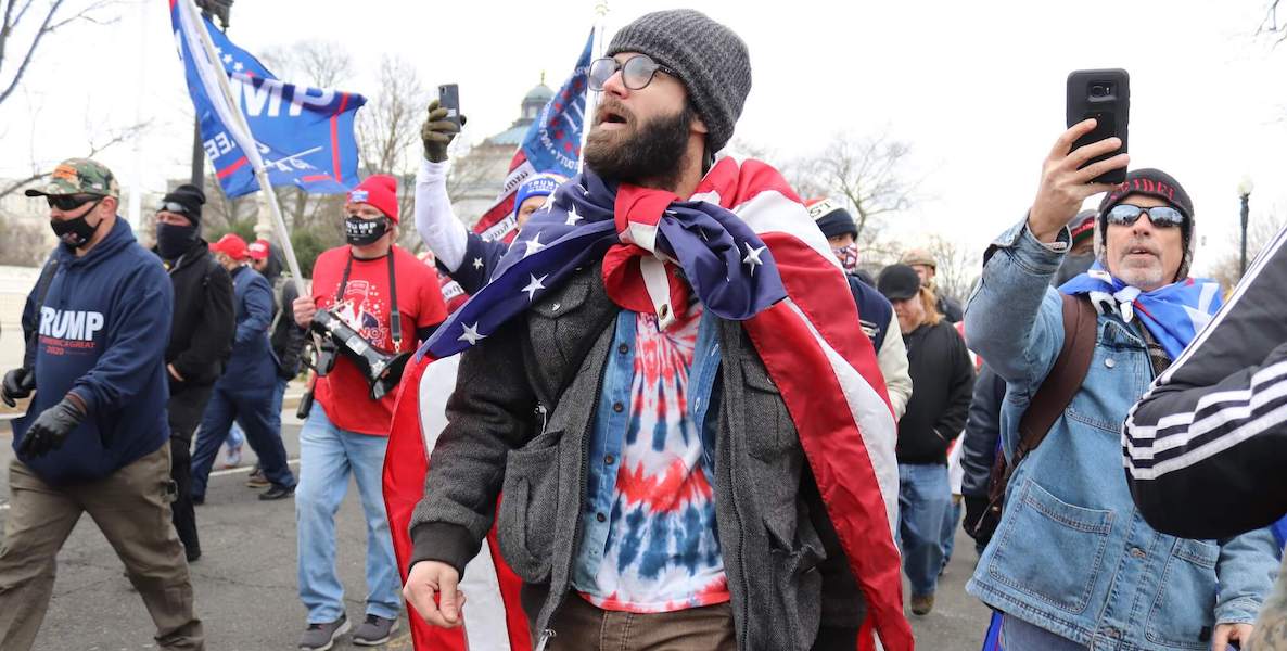 A group of Proud Boys, one of which is draped in an American flag, march on the Capitol building in Washington D.C.