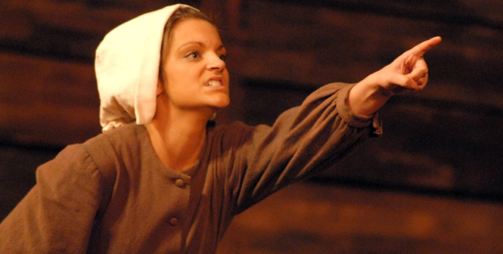 A scene from Arthur Miller's The Crucible shows a young woman pointing into the air.
