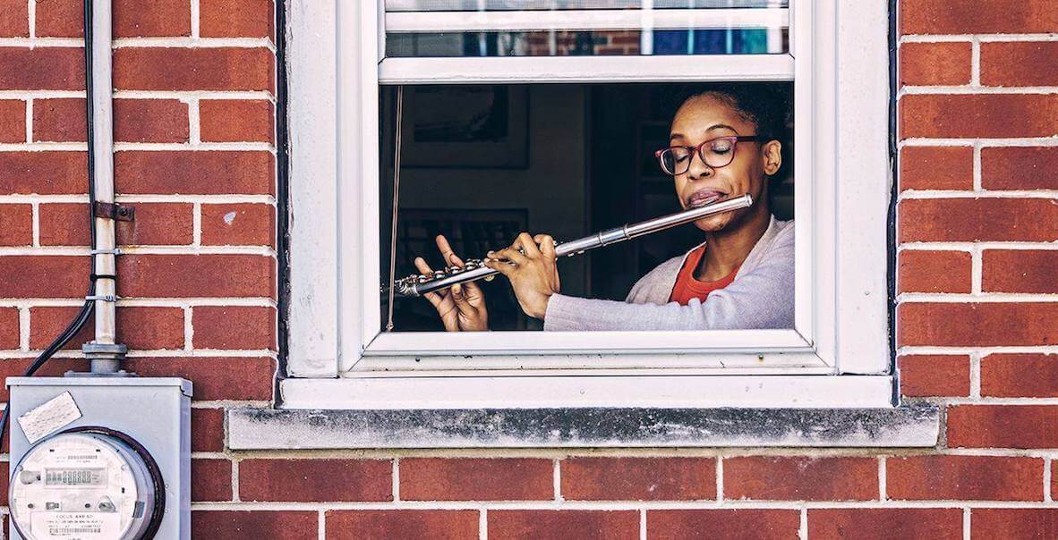 A Philadelphia woman sits at her open window, tooting on a flute for passersby