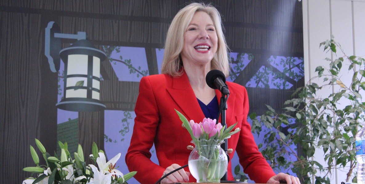 University of Pennsylvania president Amy Gutmann stands at a podium wearing a red jacket.