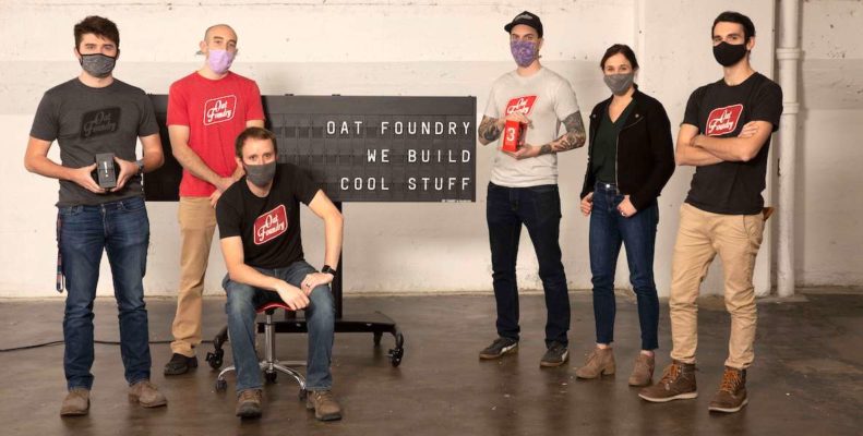 Oat Foundry employees stand next to a sign that says "We build cool things."