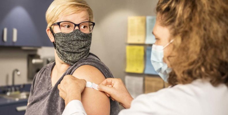 A woman wearing a mask gets a Covid vaccine from a nurse wearing a mask