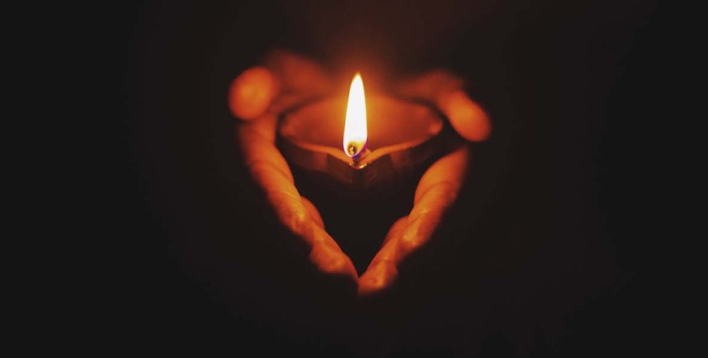 A lit candle lies in the palms of someone's hand
