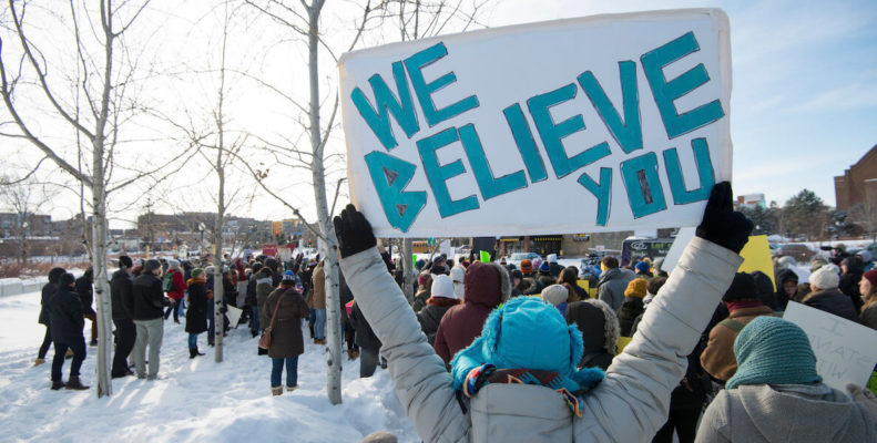 A protestor holds up a sign that reads "We Believe You" on a snowy day