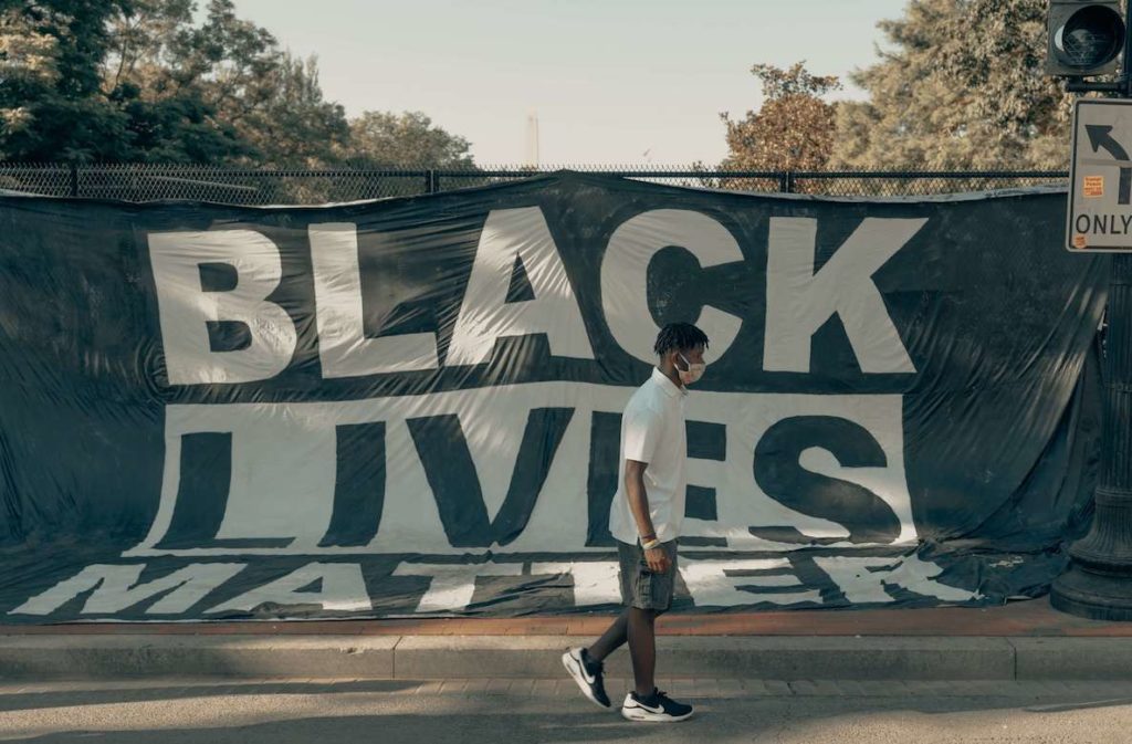 A young man walks in front of a large Black Lives Matter banner