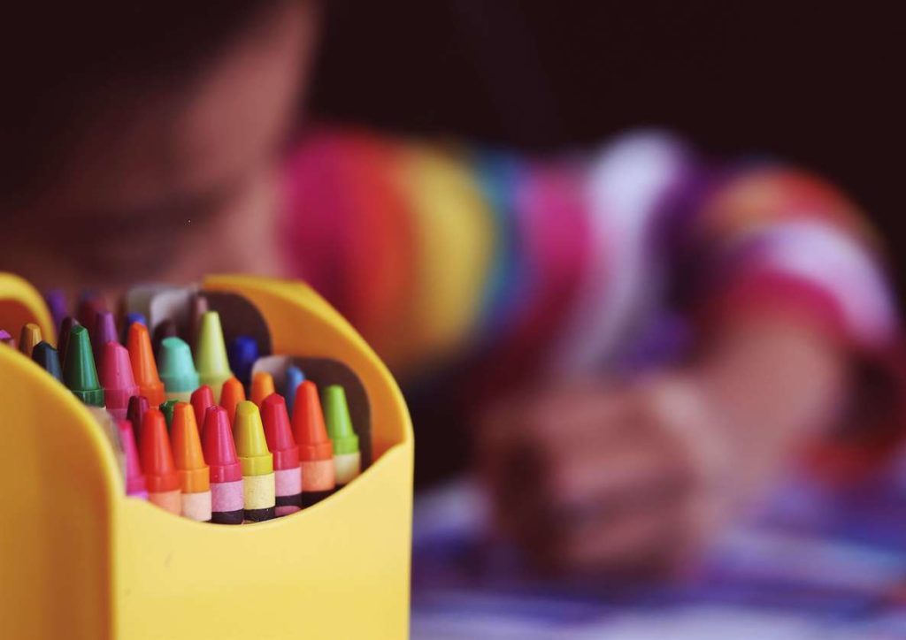 A kid uses crayons to color a picture for his parents