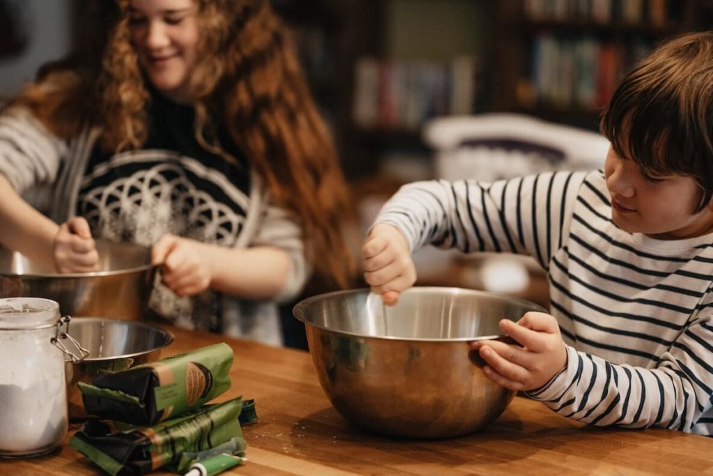 Two kids stir things in bowls to bake a cake for their mom