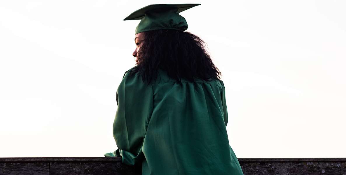 A Black graduate looks over a ledge on graduation day, envisioning all the exciting possibilities that await