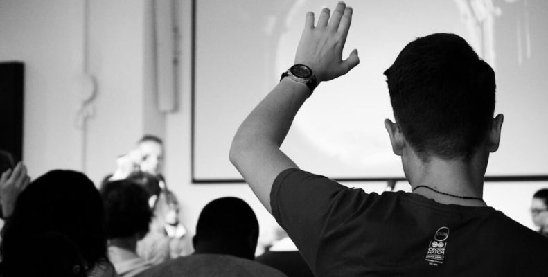 Black & white image of student raising hand in class