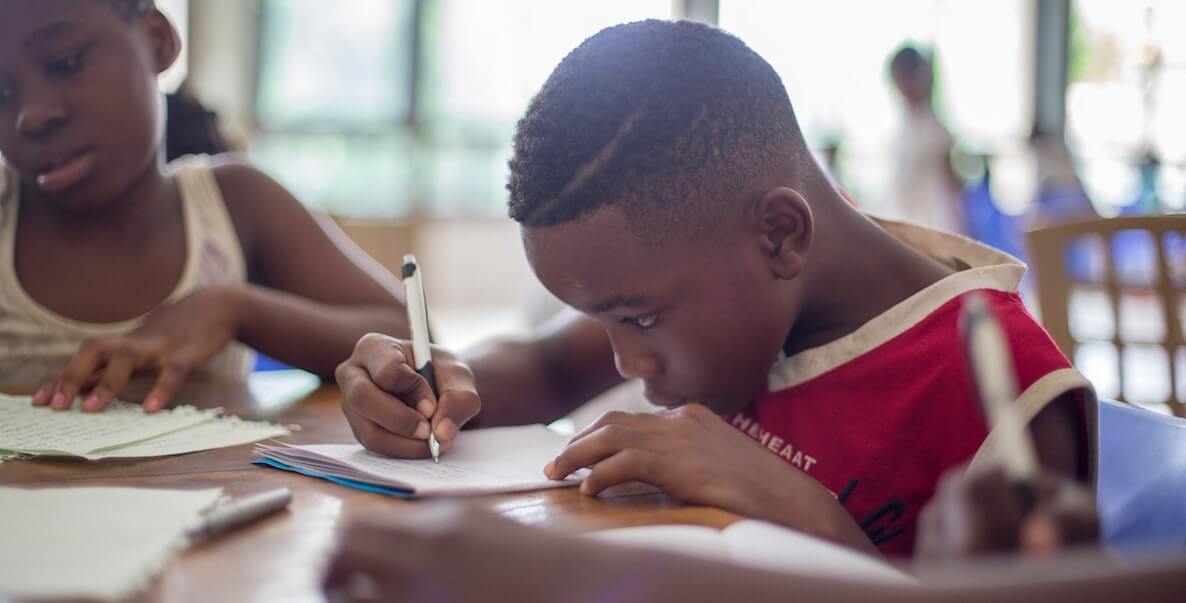 Young Black boy writing with pencil at school