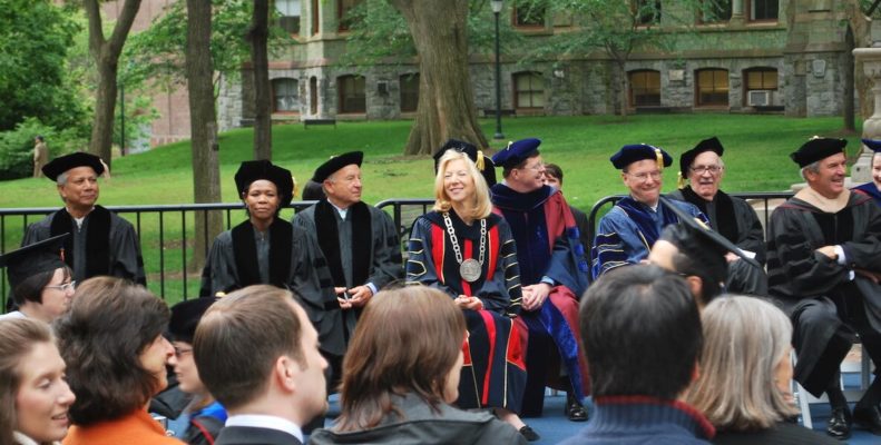 Penn president Amy Gutmann walking across the stage in a cap and gown, watching the commencement procession