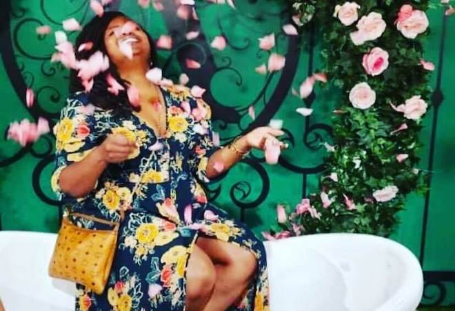 Celeste Kenton, a Black woman, wears a floral dress and sits on a white seat while flower petals drift in the air in front of her. This is a photo for C Silhouette, her veteran-owned business.