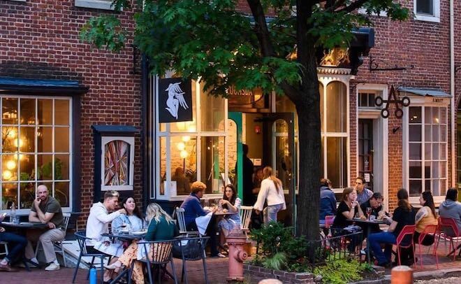 People sit at cafe tables outside a brick facade of a restaurant on Headhouse Square in Philadelphia. This is Bloomsday Cafe.