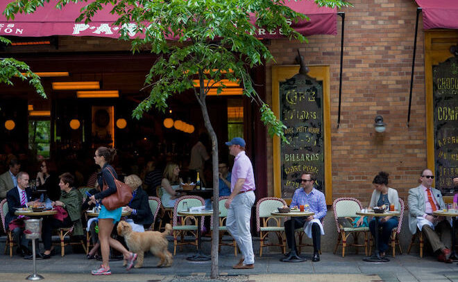 People walk by outdoor cafe tables, where more people sit, at Parc restaurant on Rittenhouse Square in Philadelphia.