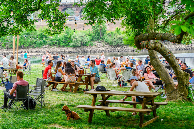 A crowd of people sit on the grass and at picnic tables on the bank of the Schuylkill River in Philadelphia, where there are so many things to do.