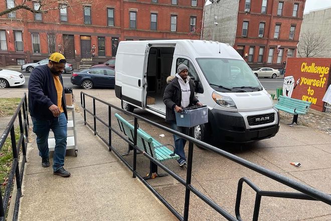 Brent Johnstone and Akeiff Staples, the co-founders of FathersRead365, transfer supplies from a white van to a cafeteria for their presentation at Tanner G. Duckrey School in North Philadelphia.