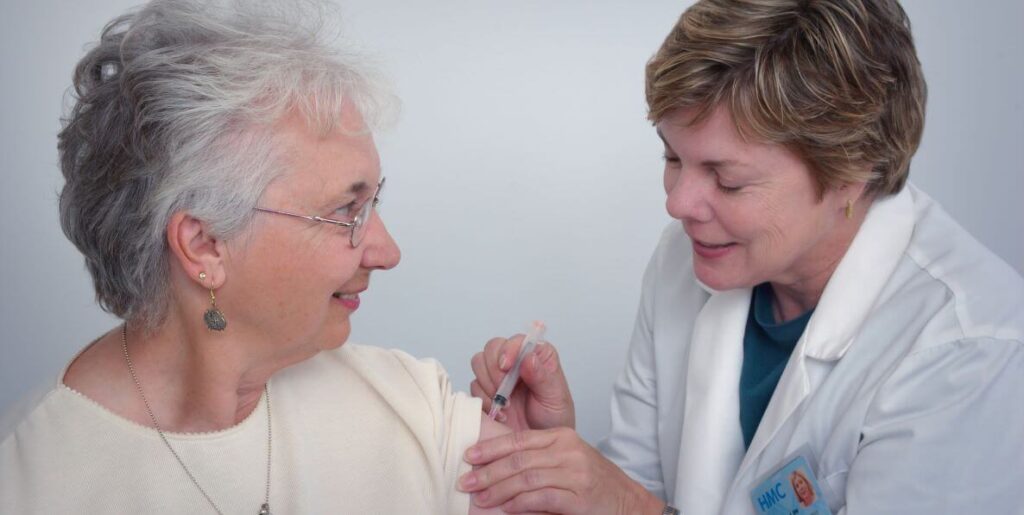 A primary care doctor administers a shot to an older woman patient