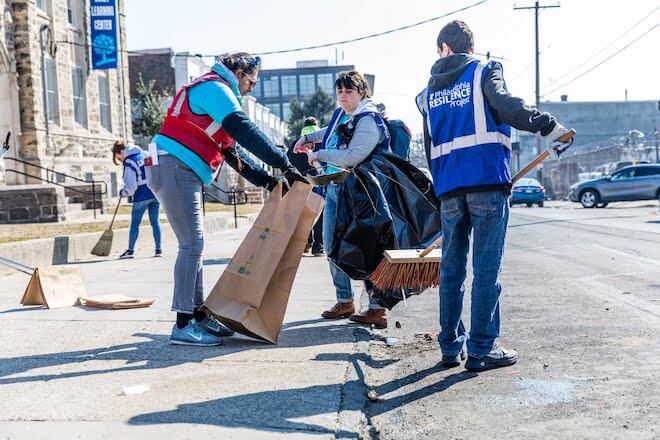 Philadelphia Resilience Project volunteers in vests clean the street and sidewalk. 