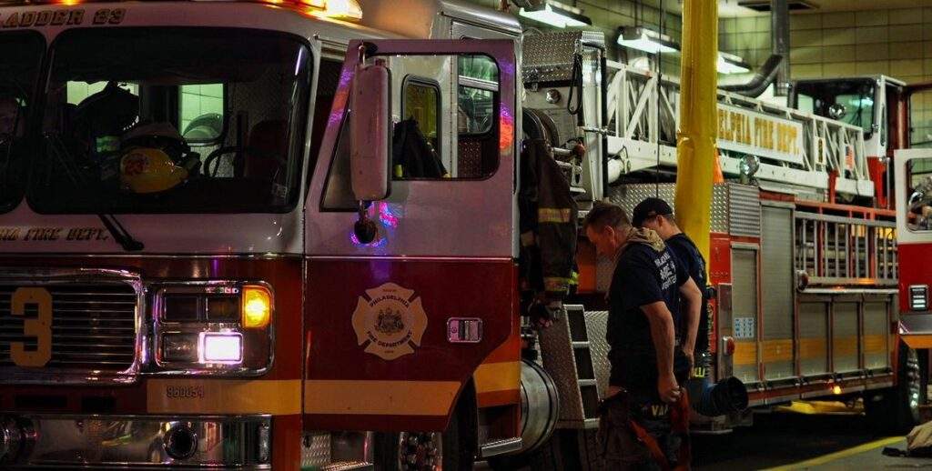 Two Philadelphia fire fighters stand beside a ladder truck with an open door