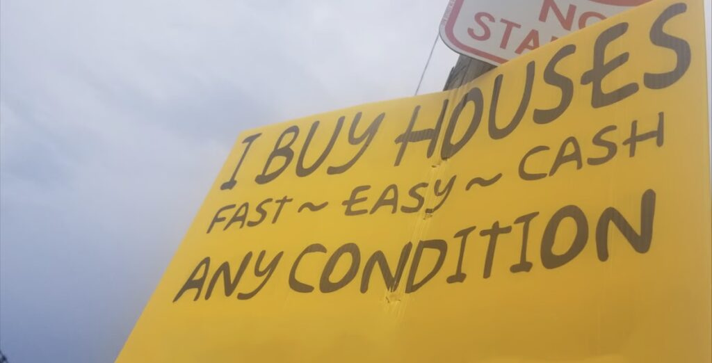 A yellow "I buy houses fast easy cash any condition" sign, another iteration of the We Buy Houses informal market that costs homeowners millions