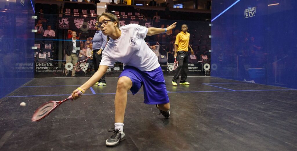 A young woman lunging forward, playing squash.
