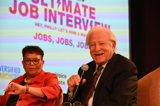 Della Clark of The Enterprise Center looks at her watch as Jim Gardner holds a microphone and laughs at The Philadelphia Citizen's Ultimate Job Interview.
