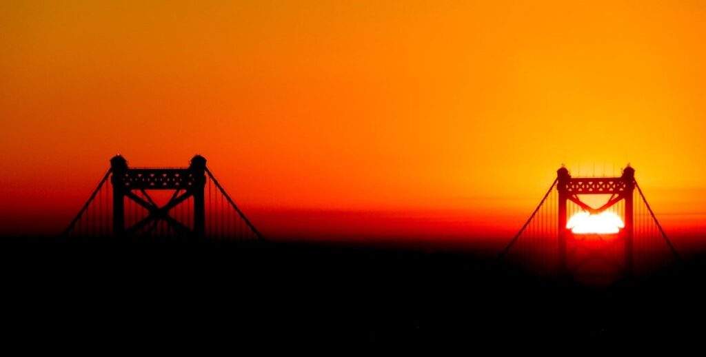 An orange sunrise with the Benjamin Franklin Bridge, Philadelphia, emerging from the dark of the night.