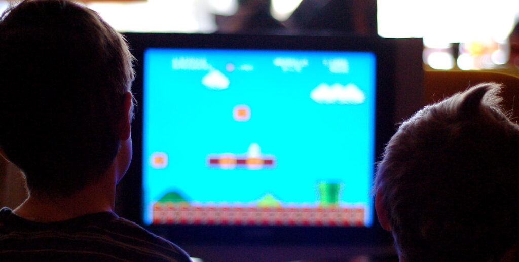 The silhouettes of two children playing a video game on a computer.