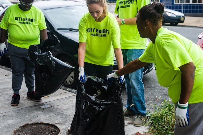 Three people work together to put trash into a garbage bag.